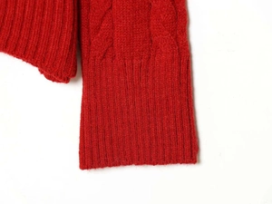Close-up of red cable knit sweater showing textured weave and ribbed elastic cuffs