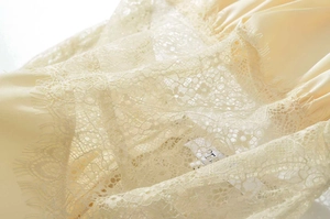 Detailed macro view of delicate eyelash lace trim on premium cream satin dress fabric