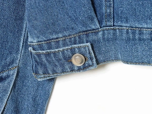 Close-up of denim jacket hem with silver metal button and contrast yellow stitching