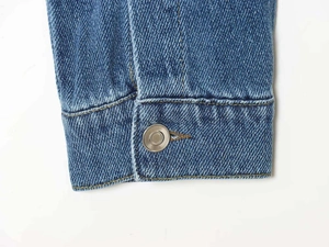 Macro detail of blue denim jacket cuff with metal button and yellow contrast stitching