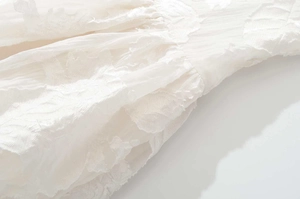 Close-up of white summer dress featuring intricate floral embroidery and textured lace fabric