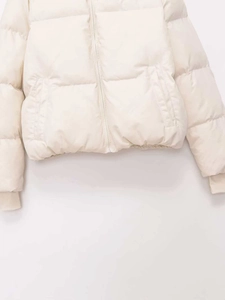 Detail of cream beige quilted jacket showing front zipper, pockets and ribbed cuffs