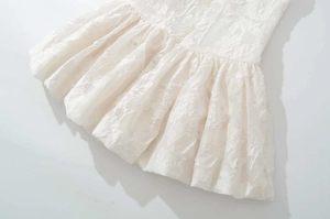 Detail of white V-neck dress with intricate floral embroidery and tiered texture