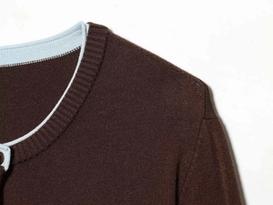 Detail of dark brown knit cardigan with light blue trim and round neck button closure