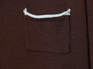 Detailed macro shot of the brown knitted cardigan pocket with decorative white wavy edges