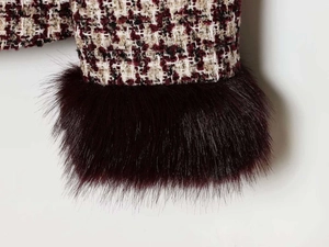 Close-up of tweed jacket cuff featuring burgundy plaid fabric and faux fur trim detail