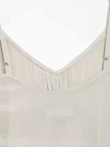 Detail of adjustable spaghetti straps and metal rings on a light beige V-neck camisole