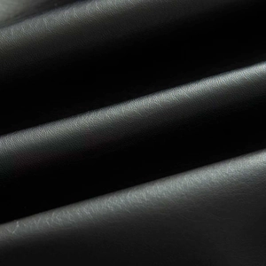 Close-up detail of premium black matte faux leather fabric with textured grain and soft folds