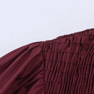 Macro detail of smocking and shirring textures on a burgundy women's blouse