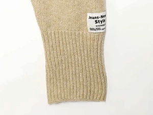Detailed close-up of knit ribbed cuff and brand label on a beige winter jacket