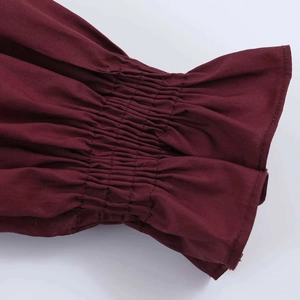 Macro detail of smocked elastic cuffs and ruffled edges on a dark red textured shirt