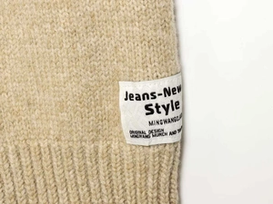 Detail of beige chunky knit fabric with a white rectangular decorative logo patch
