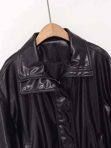 Close-up of black PU leather jacket featuring metallic snap buttons and silver zipper detail