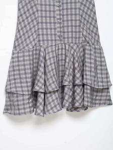Close-up of gray plaid dress featuring layered ruffle hem and button-down details