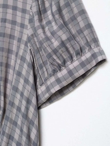 Detailed close-up of gray plaid fabric with pleated sleeve cuffs and fine stitching details