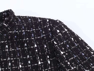 Close-up of black tweed fabric texture with metallic thread on the blazer shoulder
