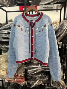 Détail du cardigan en maille bleue avec broderie florale et ruban de bordure contrasté
