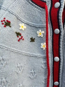 Détail de broderie florale et bordure rayée sur un cardigan en tricot bleu clair doux