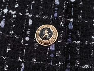 Detail of tweed blazer fabric with a gold lion head embossed metal button accessory