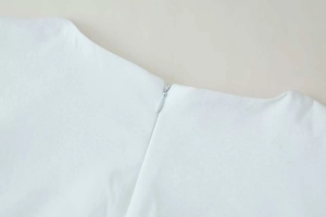 Detailed view of back invisible zipper on white sleeveless dress with textured fabric