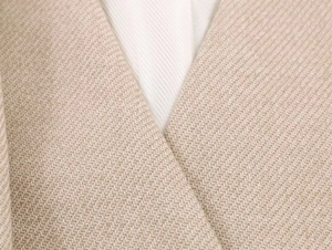 Dettaglio del tessuto testurizzato beige e del collo a sciarpa su un blazer a maniche lunghe