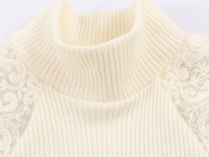 Dettaglio del top in maglia crema con collo alto e applicazioni in pizzo floreale bianco