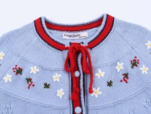 Détail de broderies florales et bordure rouge sur cardigan en maille bleu clair