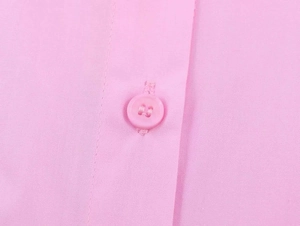 Macro detail of a pink poplin shirt featuring matched buttons and fine stitching texture
