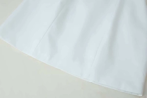 Detailed view of the straight hemline and vertical stitching on white woven dress