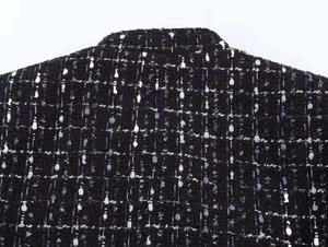 Macro detail of black tweed jacket featuring woven texture with white and lilac threads