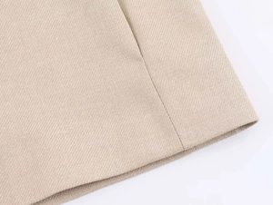Dettaglio macro della trama in saia beige e cuciture pulite sull'orlo del blazer