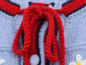 Détail macro d'un cardigan en maille bleue avec broderie marguerites et cordon rouge