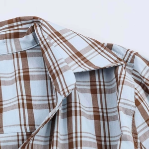 Detail shot of the light blue and brown plaid pattern poplin shirt collar and shoulder seam