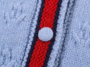 Détail macro du gilet en maille avec rayures bleu-rouge et boutons recouverts de tissu