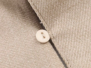 Macro del tessuto blazer beige a spina di pesce con dettaglio del bottone a due fori