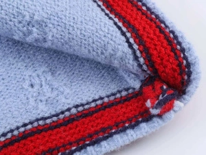 Gros plan du cardigan en tricot bleu clair avec bordures contrastées rouge et noir