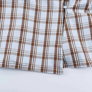 Detail of brown and white checkered poplin fabric showing a white button and stitching