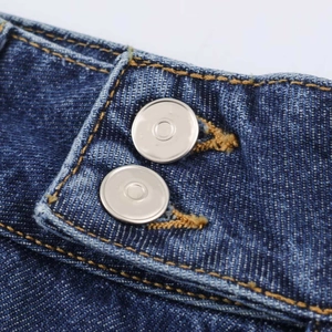 Detailed macro view of the dark blue denim waist with double silver metal buttons