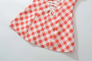 Detail of red gingham dress featuring white criss-cross lacing and silver eyelets