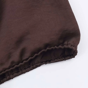 Close-up detail of dark brown satin shirt featuring elasticized cuffs and fine stitching