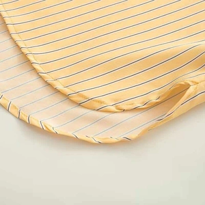 Detail of warm yellow striped shirt showing curved hemline and side slit craftsmanship