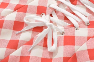 Detail of red gingham dress showing silver eyelets and white drawstring bow tie