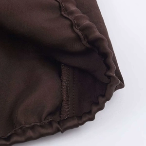 Detail of elastic cuff on dark brown satin shirt with clean overlock stitching quality