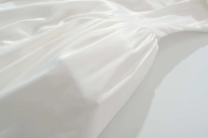 Vue macro détaillée du tissu satiné blanc perle plissé montrant la texture lisse sur la robe