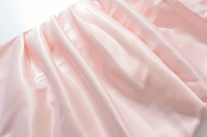Vista dettagliata del tessuto satinato rosa chiaro con drappeggio elegante e lucido