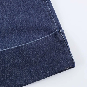 Close-up of deep blue denim fabric with rolled hem stitching and twill texture