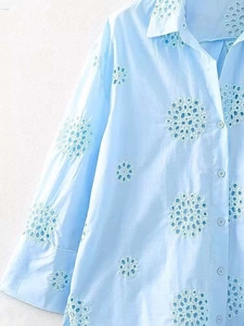 Detail of light blue shirt featuring floral eyelet embroidery and resin buttons