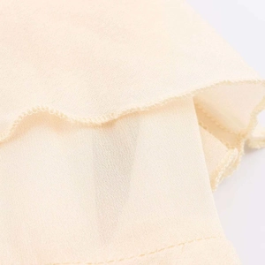 Detail of light beige chiffon fabric showing multi-layer drape and fine rolled hem stitching