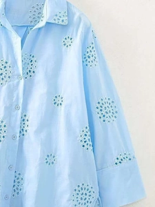Detail of light blue shirt featuring intricate floral embroidery and white buttons