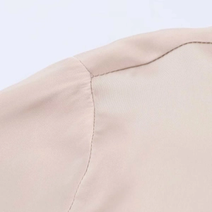 Detailed shoulder seam and collar stitching on a smooth beige satin blouse fabric